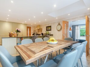 A modern kitchen with a dining area, featuring a wooden table, blue chairs, and a clock on the wall.