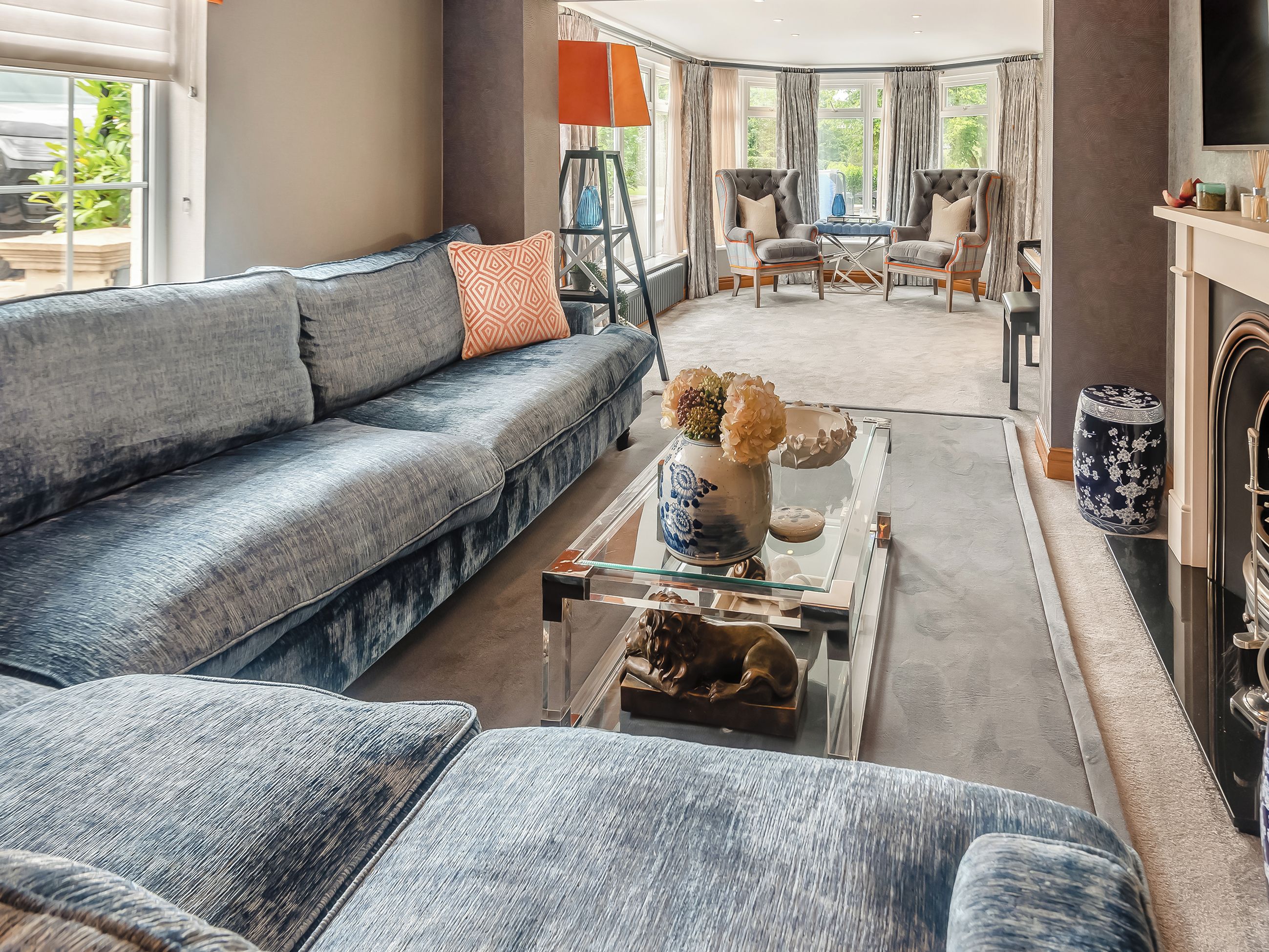 A modern living room with a grey sofa, a glass coffee table, and two armchairs.