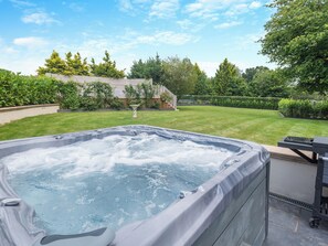 A hot tub in a backyard with a lawn, trees, and a wooden fence.