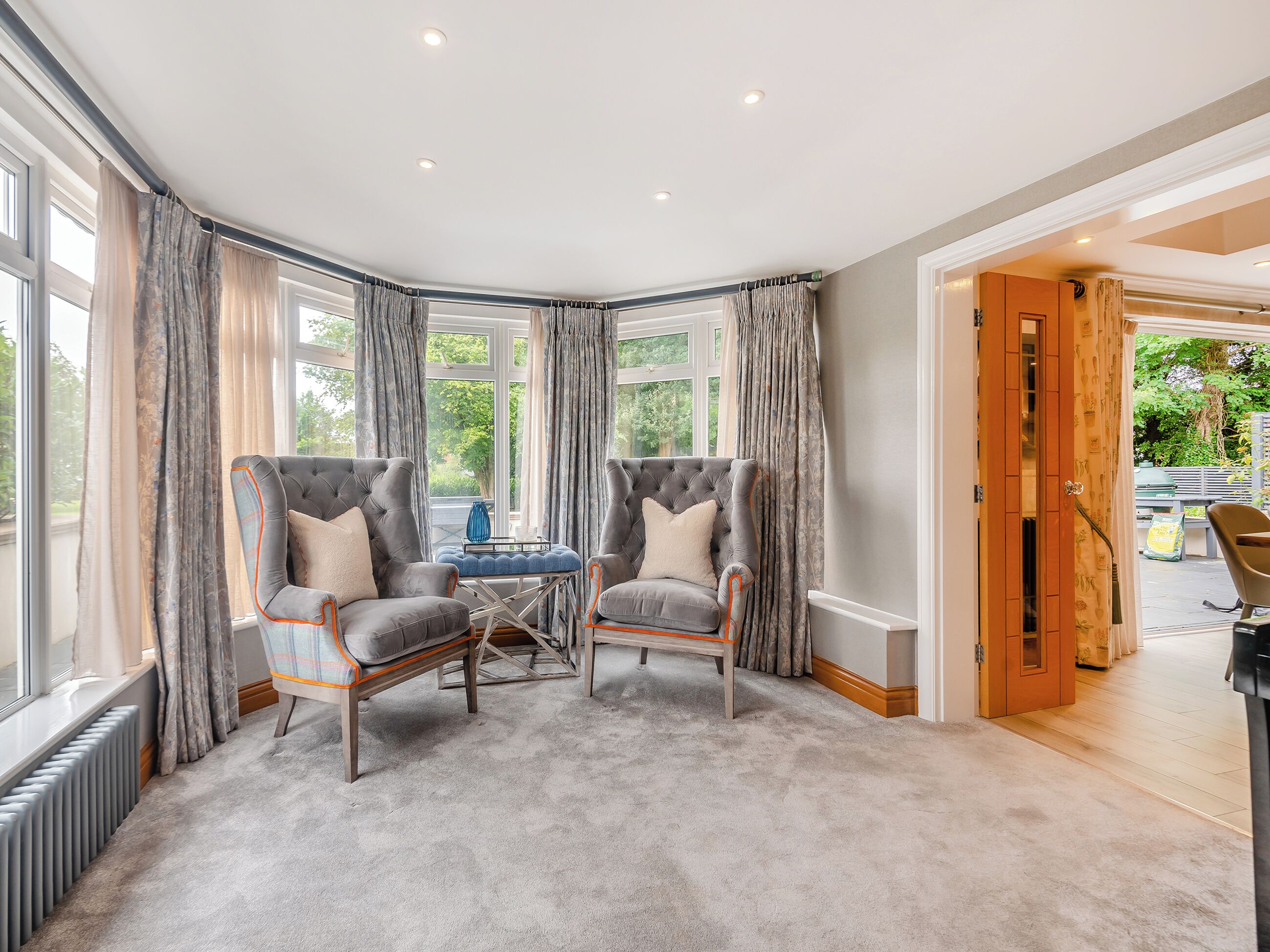 A corner room with two armchairs, a small table, and a view of the outdoors through large windows.
