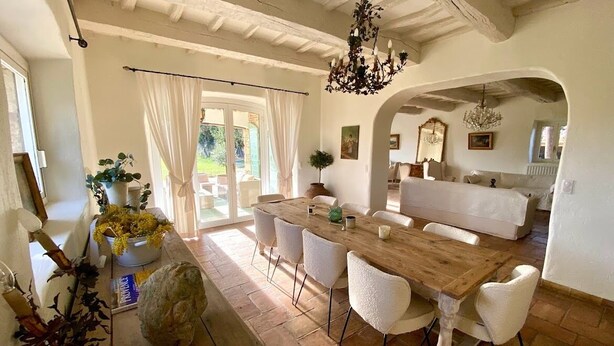 A dining area with a wooden table and white chairs, a chandelier, and a view of the outdoors. - Mas Provençale Entouré de Pommiers, Piscine et Terrain de Tennis (Cavaillon)