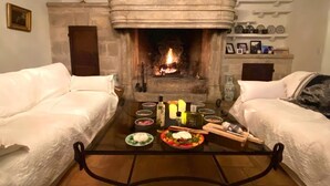 A cozy room with a fireplace, two white sofas, a glass coffee table with food and drinks, and a stone fireplace surround. - Mas Provençale Entouré de Pommiers, Piscine et Terrain de Tennis (Cavaillon)