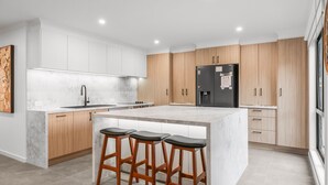 A modern kitchen with a marble countertop, wooden cabinets, a black refrigerator, and three bar stools. - The Beach House on Pembrey (Cowes)
