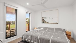 A bedroom with a large bed, a ceiling fan, a sliding glass door, and a framed picture on the wall.