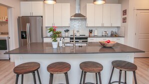 Une cuisine moderne dotée d’un îlot central, d’appareils électroménagers en acier inoxydable, de meubles blancs et de tabourets de bar.