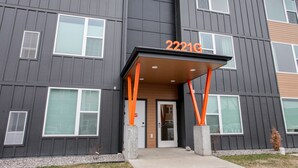 Un immeuble à plusieurs étages, doté d’une architecture moderne, se distingue par son entrée imposante, avec des piliers structurels orange, et une enseigne affichant le numéro 2221.