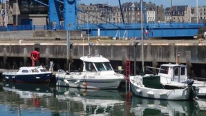 Un port avec des bateaux amarrés, une grande grue bleue et des bâtiments en arrière-plan.