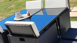 Un espace extérieur aménagé pour les repas, avec une table bleue et des chaises en osier, un parasol et une vue sur un paysage verdoyant.