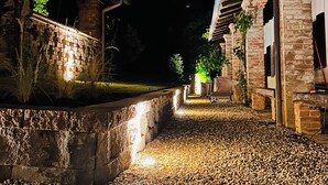Ein beleuchteter Außenweg bei Nacht, mit Steinmauern und Holzkonstruktionen.