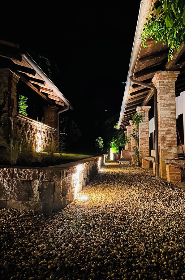 A nighttime outdoor pathway with stone walls and wooden structures, illuminated by ground lights. - Cascina Bella Relais: An Oasis of Luxury and Tranquility (Piemonte)