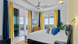A modern bedroom with a large bed, a ceiling fan, and a view of the outdoors.