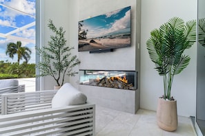 Un salon moderne avec un téléviseur à écran plat, une cheminée, une grande plante en pot et un canapé blanc.