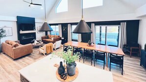 A spacious living area with a large wooden dining table, a sofa, and a TV. - Lux Lake View Retreat: Table Rock View, Hot tub, Pool, Pet Friendly (Hollister)