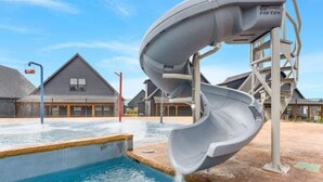 A water slide structure over a pool with a clear sky and residential buildings in the background. - Lux Lake View Retreat: Table Rock View, Hot tub, Pool, Pet Friendly (Hollister)