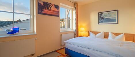 A hotel room with a bed, a window with a view, a lamp, and a painting on the wall.