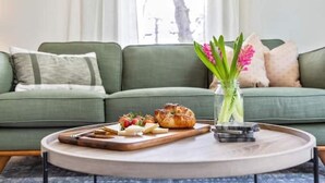 A green sofa with a tray of food and a vase of flowers on a round table. - New England Charm, Portland - Parking included (Portland)