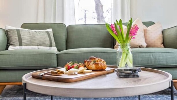 A green sofa with a tray of food and a vase of flowers on a round table.