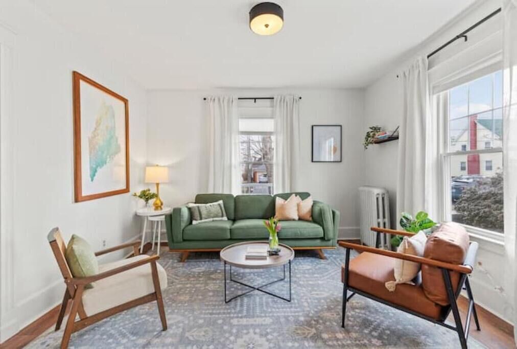 Una sala de estar con un sofá verde, una silla de madera, una mesa de centro y vistas al exterior a través de una ventana.