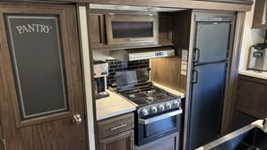 A compact kitchen with a stove, oven, microwave, and refrigerator. - 26FT CAMPER IN THE BEST FISHING/HUNTING SECRET IN SC (Iva)