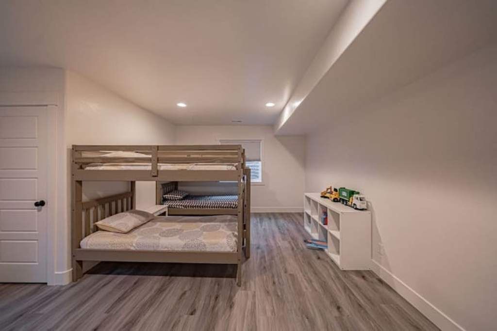 A bunk bed in a room with a wooden floor, a white door, and a small white shelf with toys.