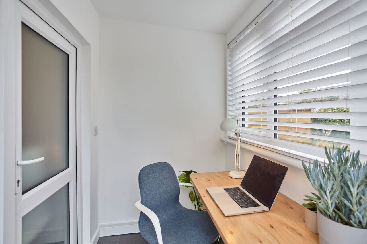 A modern office space with a desk, chair, laptop, and window blinds.