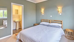 Ein Schlafzimmer mit Bett, Nachttisch, rundem Korbstuhl und einem Badezimmer mit Waschbecken und Spiegel.