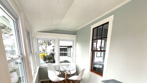 A bright room with a wooden floor, a round glass table, and white chairs. - Adorable beach house - 5 min walk to private beach (Wareham)