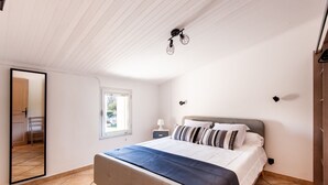 Een slaapkamer met een bed, een raam, een nachtkastje, een spiegel en een kledingkast.