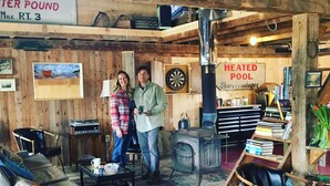 A rustic interior with wooden walls, a dartboard, a heated pool sign, and a bookshelf.