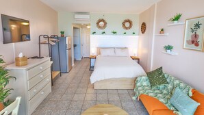Ein kompaktes Hotelzimmer mit Bett, Sofa, Fernseher, Kommode und einer Küchenzeile.
