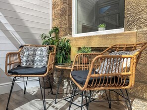 Wicker chairs with black cushions and patterned pillows, a small table, and potted plants in a sunlit corner with stone walls and a window. - 2 bedroom accommodation in Tansley (Tansley)