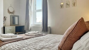 Ein Schlafzimmer mit einem Bett, einem Schminktisch, einem Fenster mit Vorhängen und Wandbildern.