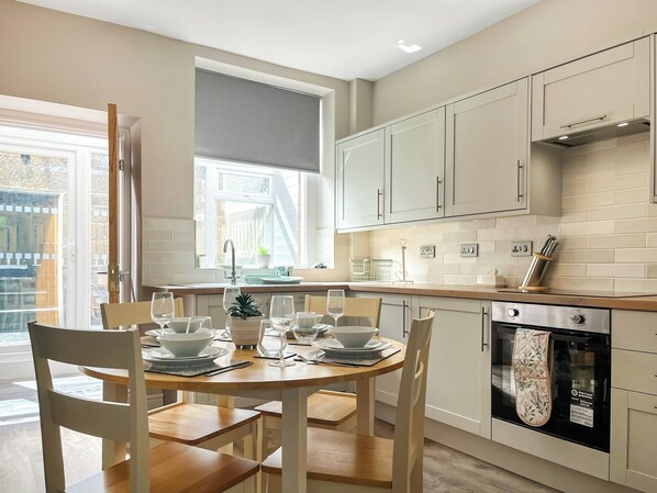 A modern kitchen with white cabinets, a wooden countertop, and a dining area with a round table and chairs. - 2 bedroom accommodation in Tansley (Tansley)