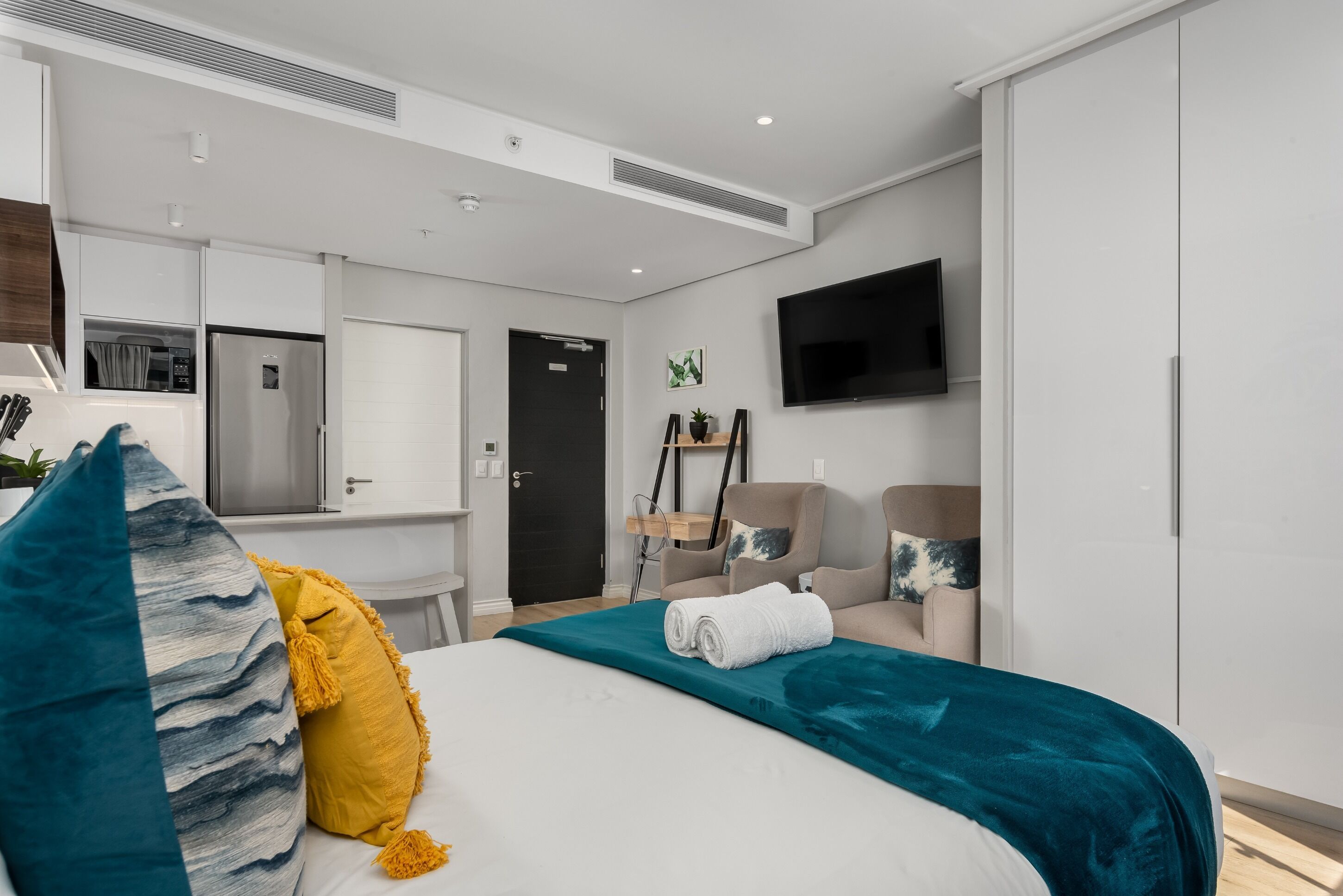 Una habitación de hotel moderna con una cama, un escritorio, una silla, un televisor y un armario.