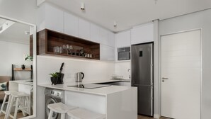 A modern kitchen with white cabinetry, a stainless steel refrigerator, a built-in microwave, and a wooden shelf. - Bright Studio With City Views - No Load-shedding (Cape Town)