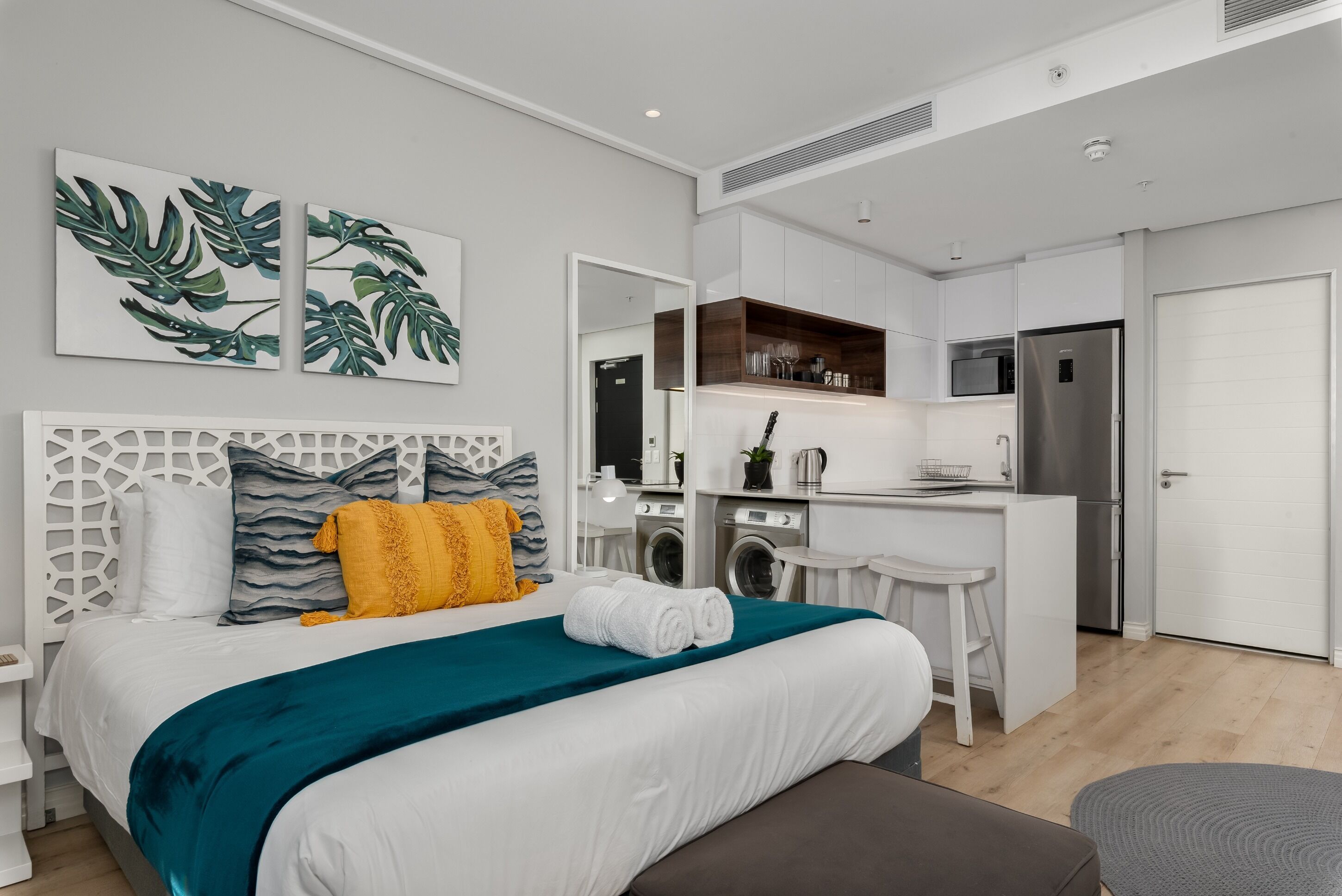 A modern hotel room with a bed, a small kitchenette, a washing machine, and a dining area.