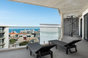 A balcony with two lounge chairs, a glass wall, and a spiral staircase. - Penthouse with Gorgeous Mountain and Ocean Views (Cape Town)