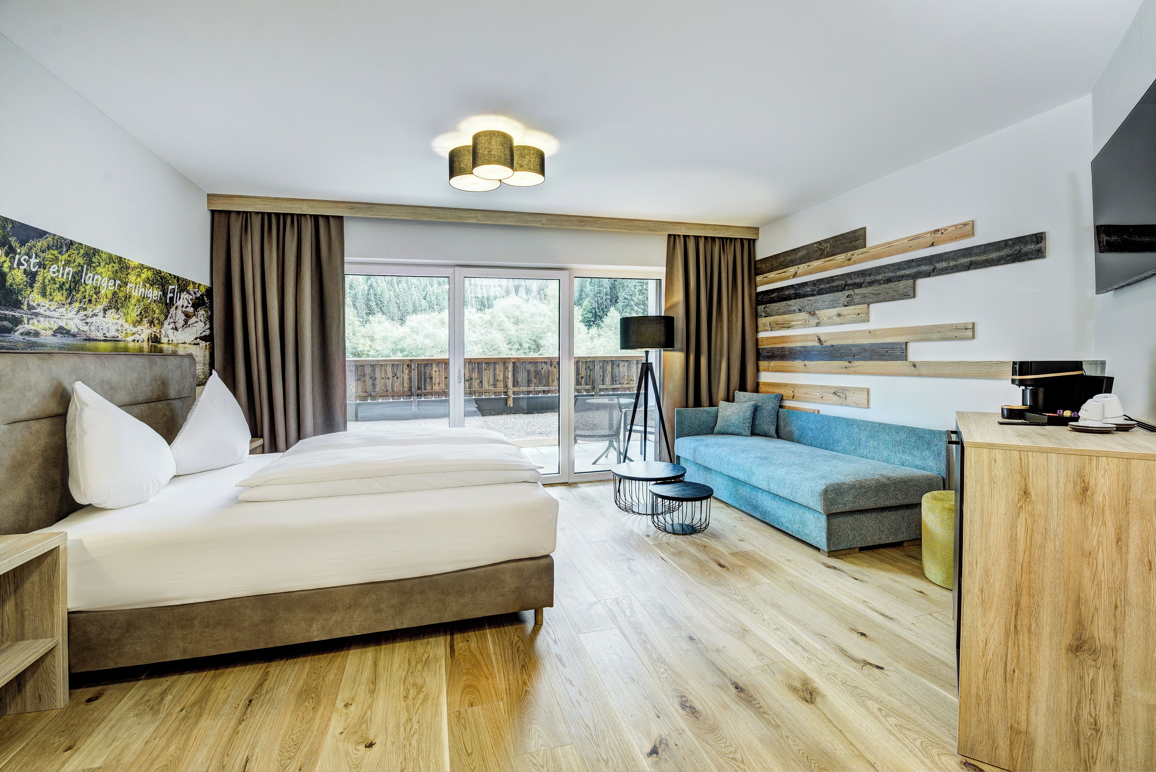 A modern hotel room with a large bed, a sofa, a desk, and a view of the outdoors.