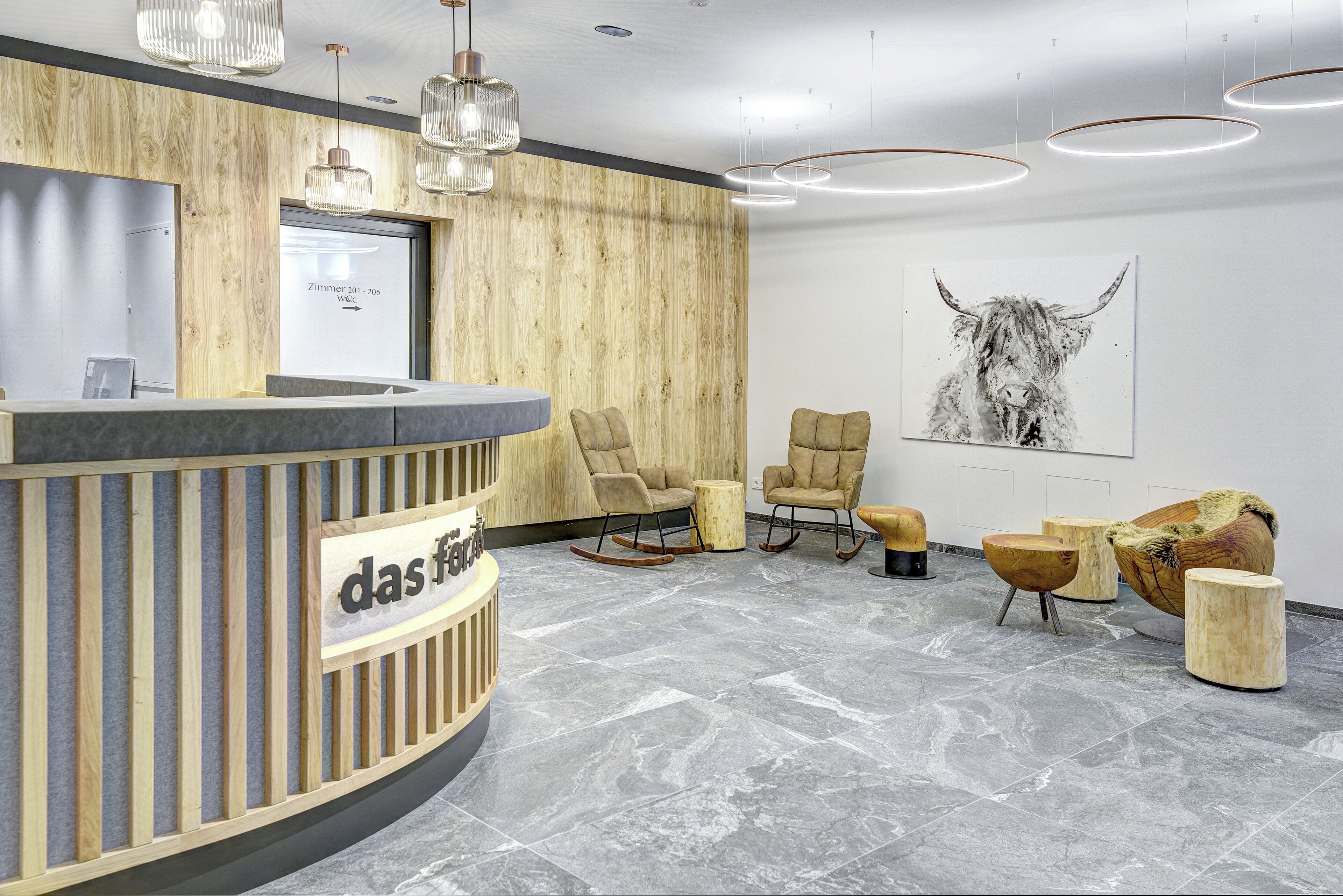 A reception area with a wooden reception desk, two rocking chairs, and a large bull painting on the wall.
