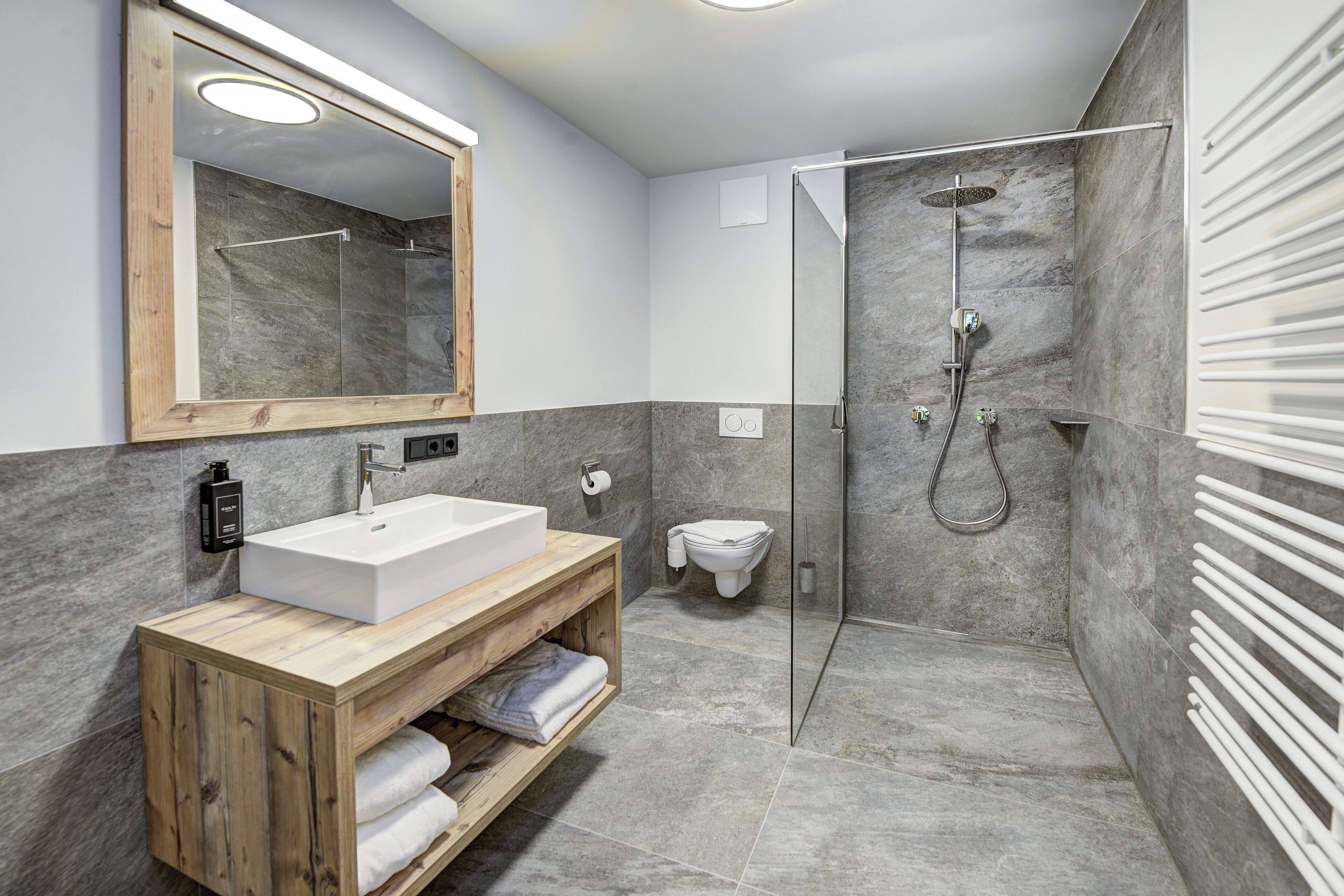 A modern bathroom with a wooden vanity, a large mirror, a shower enclosure, and a toilet.