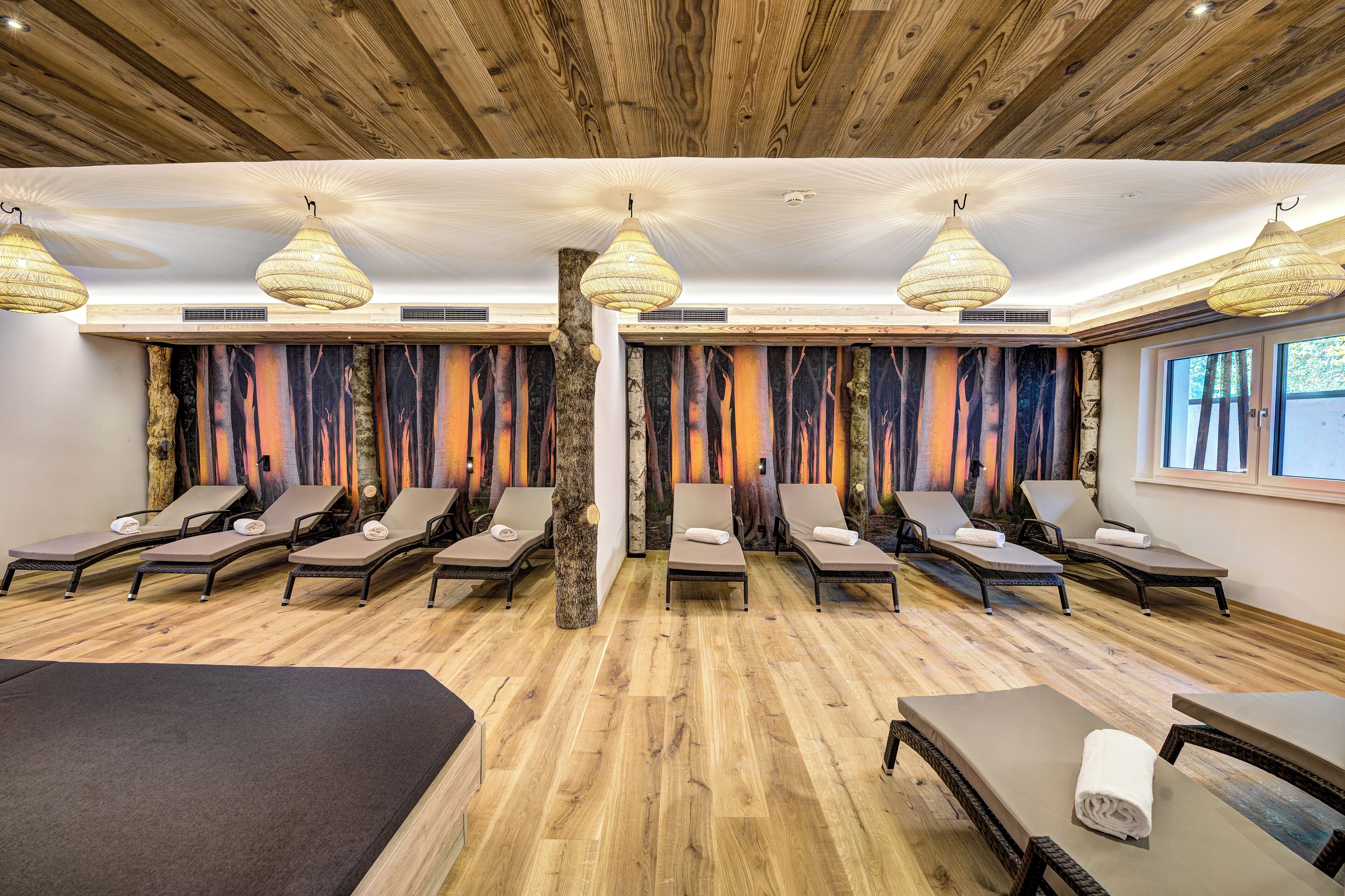 Un cuarto de spa con suelo de madera, varios camastros y un tronco de árbol como elemento central.