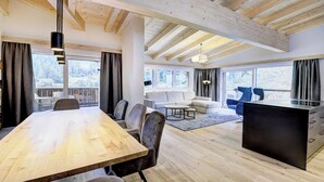 A spacious living area with a wooden dining table, comfortable seating, a sofa, and a kitchen area. - Das Förstereck (Viehhofen)