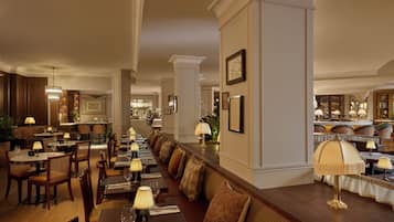 Un restaurante con mesas largas comunitarias, asientos acolchados y candelabros.