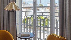 A room with two yellow chairs, a small table with a book, and a lamp. A large window with a view of the Eiffel Tower is visible. - Miiro Le Grand Hôtel Cayré (Paris)