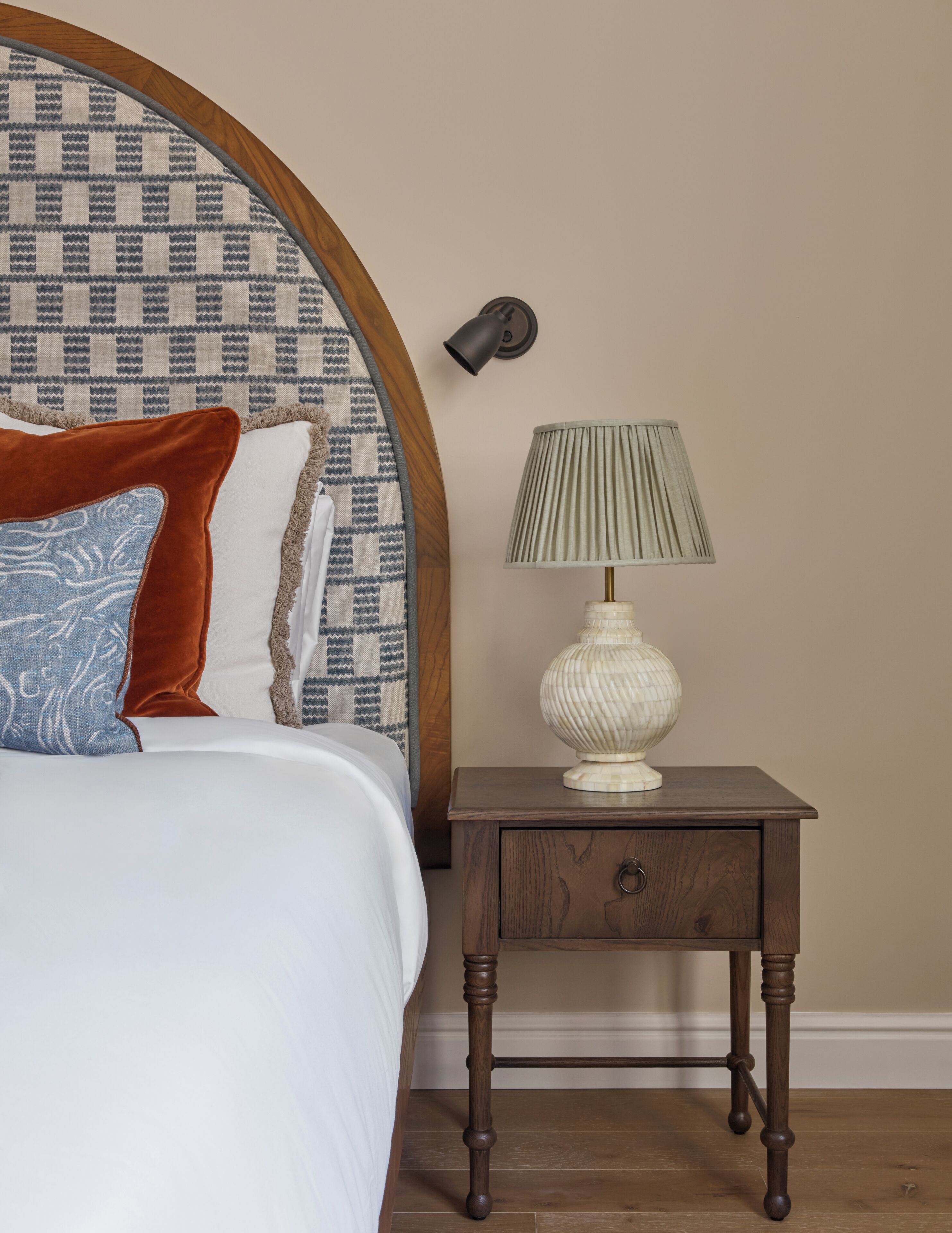 A bedroom with a patterned headboard, a bedside lamp, a nightstand with a drawer, and a bed with pillows.