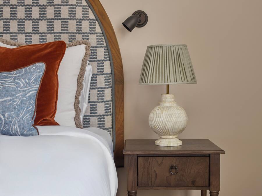 Un dormitorio con cabecera estampada, lámpara de noche, mesita de noche con cajón y cama con almohadas.