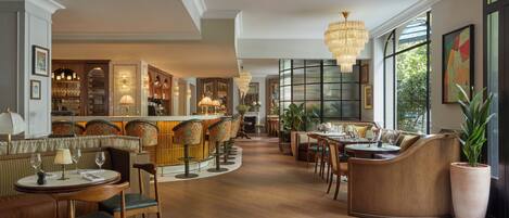 A spacious hotel lobby with a bar area, seating arrangements, and large windows providing natural light.