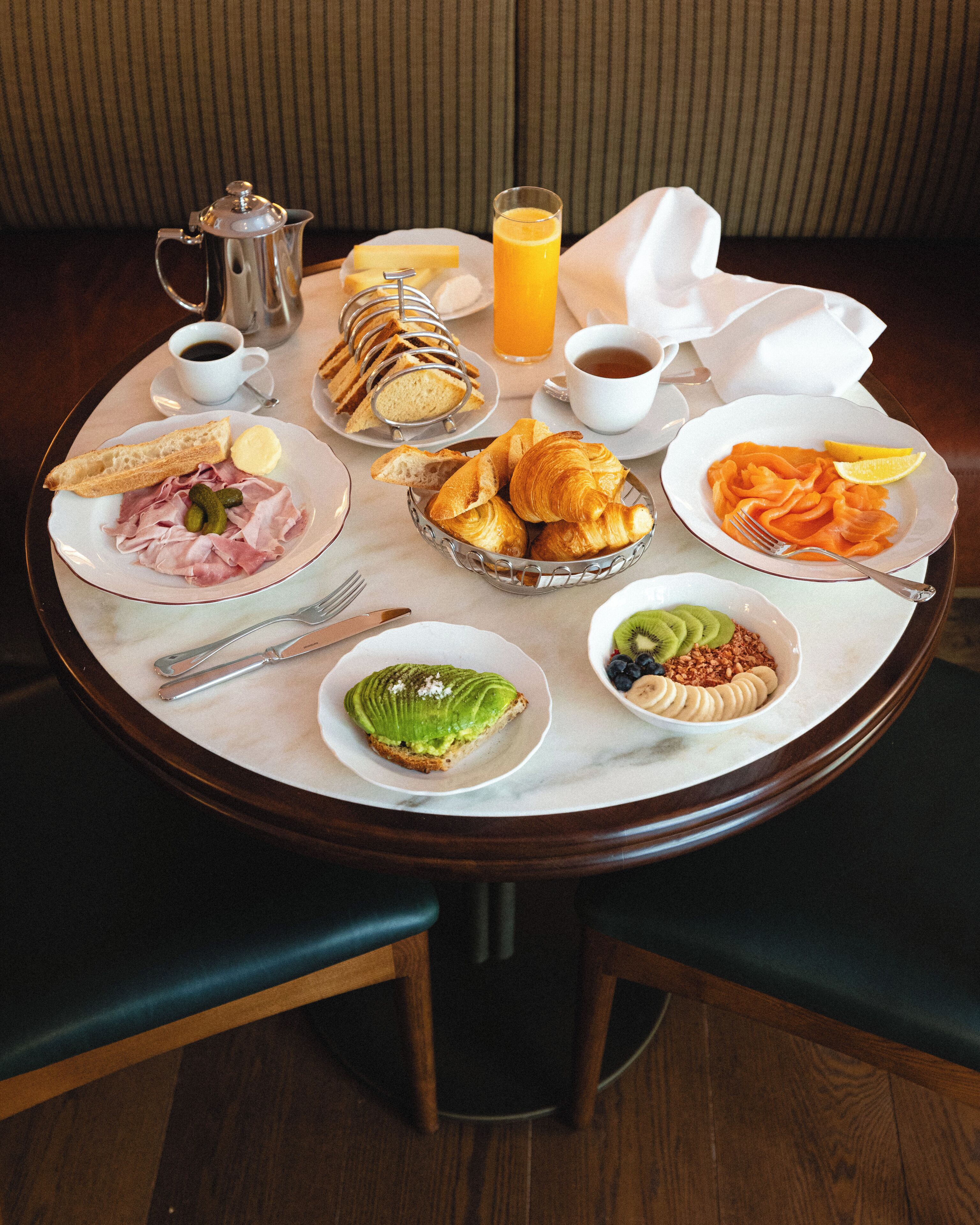 Une table de petit-déjeuner avec divers plats, notamment des croissants, du saumon fumé et des toasts à l’avocat.