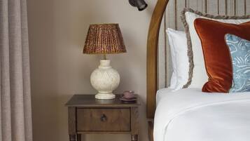 A bedroom with a wooden nightstand, a white lamp, a patterned rug, and a bed with a headboard.