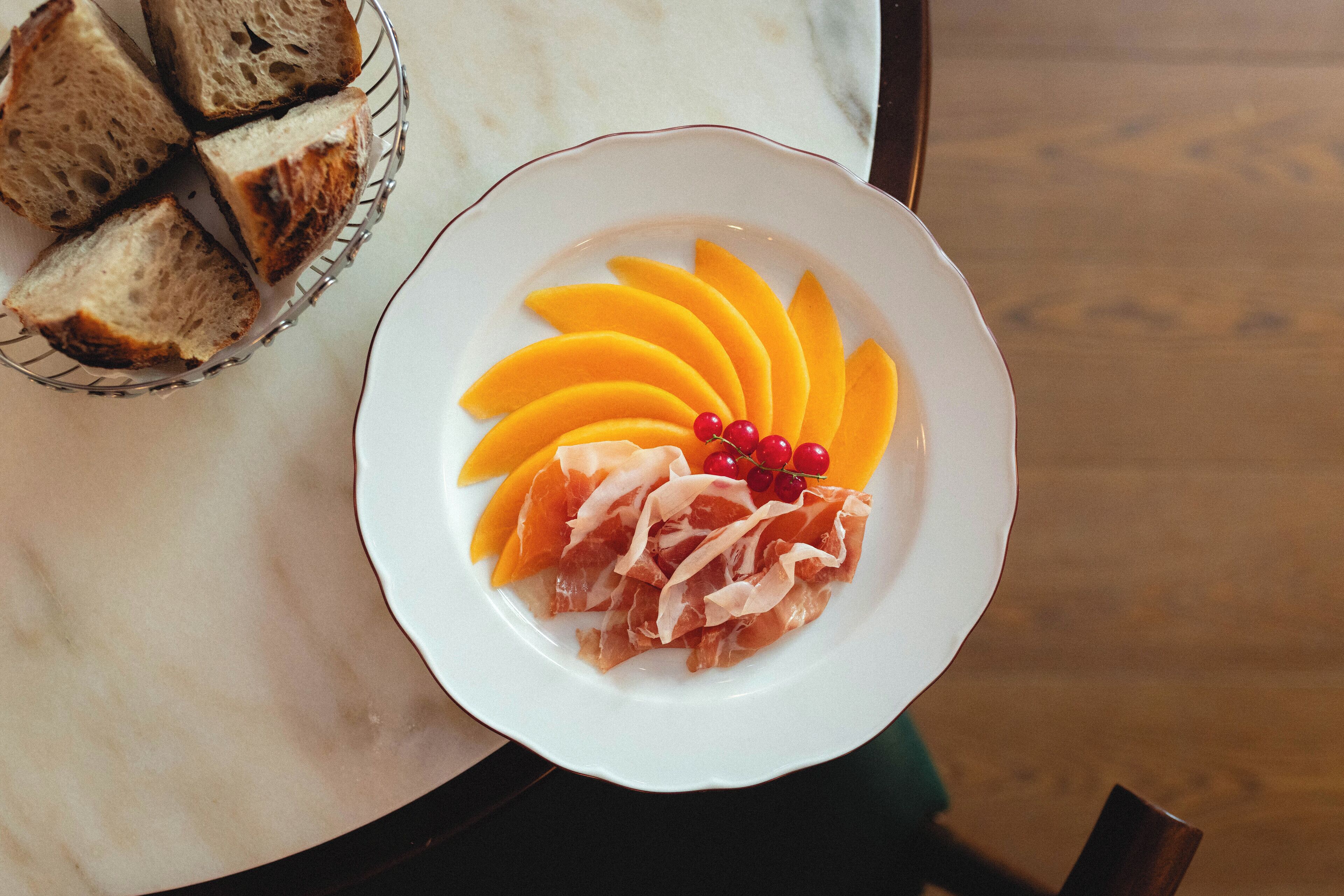 A plate with sliced mangoes, prosciutto, and red currants on a white plate.